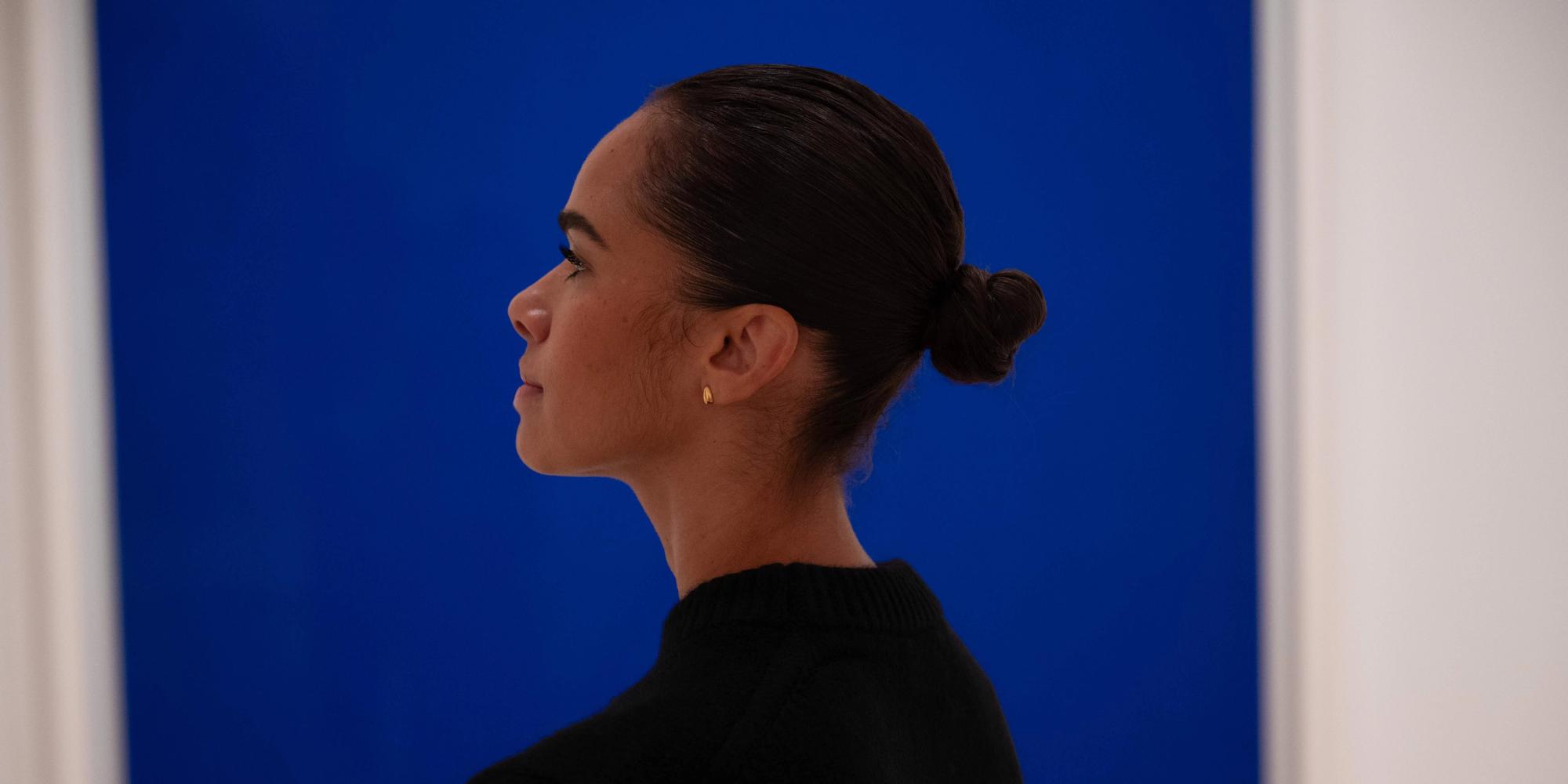 Profile view of a person standing in front of a blue painting. 